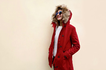 Side view of stylish smiling woman in red jacket with fur hood standing and looking away at blank...