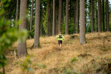 Young athlete runs uphill with a drinking backpack. Trail run in a beautiful autumn forest
