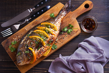 Orange ginger sea bream fish, sprinkled with sesame seeds and cilantro on serving board. Soy orange...