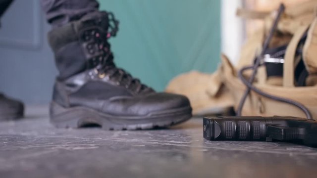 A soldier picks up a pistol and military bag from the floor and walks away. Shooting from below. Сlose up shot.