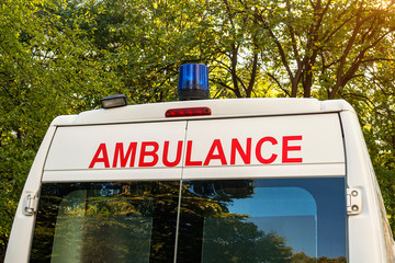 Stationary white ambulance car with a blue light on a roof. An emergency medical service van in a park. On a sunny autumn day. © Maryia