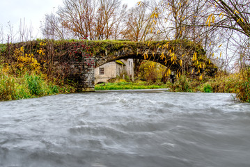 Obraz premium old stone bridge over a small fast river. time is mercilessly in man s buildings and slowly destroys buildings