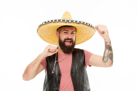 Adding hat to his spanish costume. Bearded man smiling in traditional sombrero hat. Happy hipster with beard and mustache wearing casual clothes and mexican hat. Mexican man in traditional straw hat