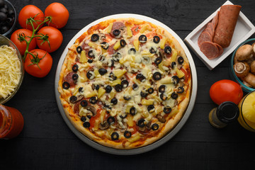 Pizza on a black background with ingredients, tomatoes, salami, mushrooms, sauce and mazzarella cheese. Italian pizza, culinary recipes concept, menu, restaurant, gourmet cuisine
