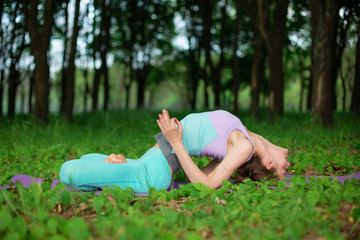 Naklejka na ściany i meble A young sports girl practices yoga in a quit green summer forest, yoga assans posture. Meditation and unity with nature