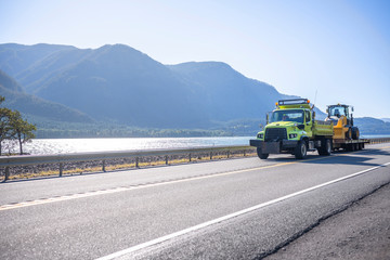 Small compact semi tip truck transporting multifunctional tractor driving on the road along Columbia River