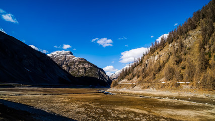 Mountain valley with stream and riverbed, trees and dried Livigno lake, Alps, Italy
