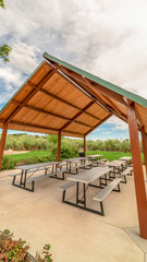 Obraz premium Vertical A small picnic pavilion at a park with view of lush foliage and cloudy blue sky