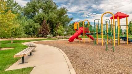 Foto op Plexiglas Panoramaframe Schilderachtig uitzicht op een park met kleurrijke kinderspeelplaats en bankjes op pad © Jason