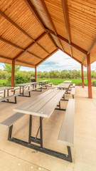 Vertical Row of white tables with seats under a pavilion with brown ceiling at a park