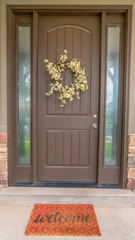 Vertical frame Flower wreath on a brown front door with sidelights and windows on both sides