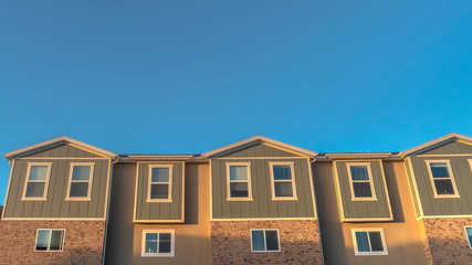 Fototapeta na wymiar Panorama Upper storey of townhomes viewed from below against blue sky on a sunny day