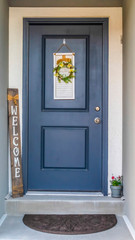 Vertical Blue front door of a home decorated with wreath welcome sign and potted flower