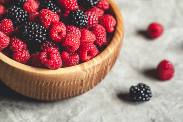 raspberries and blackberries in wood bowl on gray table, vintage