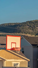 Vertical Focus on a basketball ring and board against houses on a sunny day