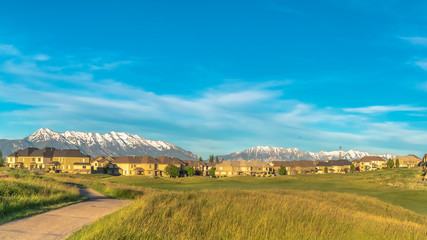 Panorama Sunny day view of pathway amid grassy ground leading to homes and golf course