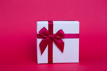 New Year's white gift with a red ribbon and bow on a red background.