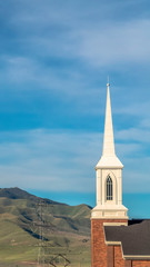 Vertical frame Rooftop and steeple of a church against power lines mountain and blue sky