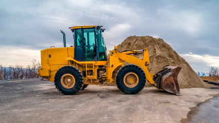 Panorama Yellow bulldozer on a road with mound of soil and cloudy sky background