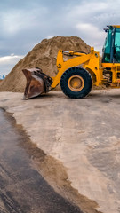 Vertical Yellow bulldozer on a road with mound of soil and cloudy sky background