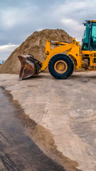 Obraz premium Vertical Yellow bulldozer on a road with mound of soil and cloudy sky background