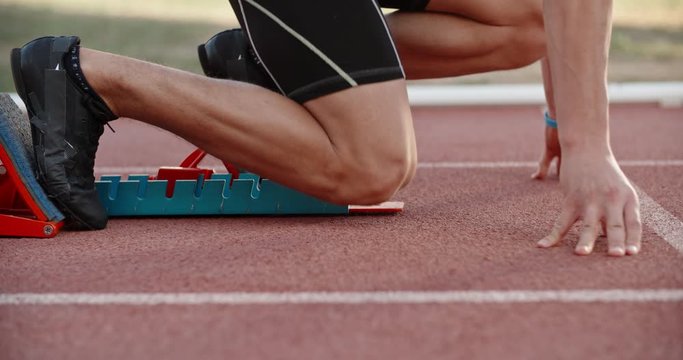 An athlete is getting ready for sprinting, putting feet in starting blocks, then blasting off - professional sports concept 4k footage
