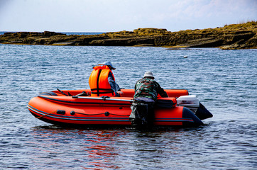 Two people at a rubber boat with a motor off the seashore.