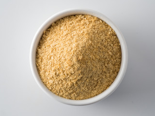 Nutritional yeast background. Nutritional inactive yeast in small white ctramic bowl. Copy space. Top view. Nutritional yeast is vegetarian superfood with cheese flavor, for healthy diet