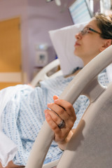 mother in hospital bed pregnant and in labor, holding on to bed rail in pain, wedding rings showing