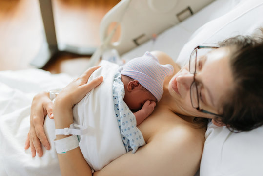 newborn baby in hospital after just being born, mother holding him and breastfeeding in hospital bed
