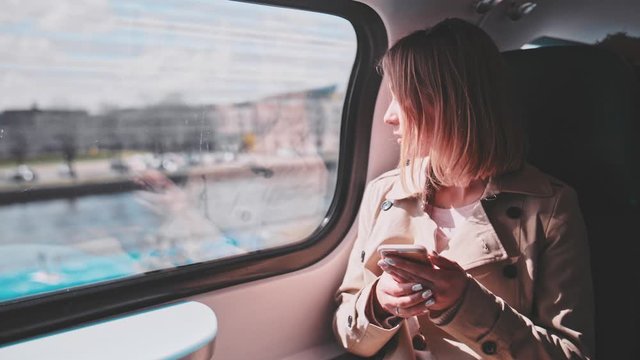 Young Woman Using Smartphone on a Train. SLOW MOTION. Business woman Looking Out of a Train Window during her daily commute, using cell phone. Social network, planning, communicating.
