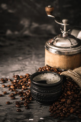 Coffee cup with coffee grinder and coffee beans on dark textured background.