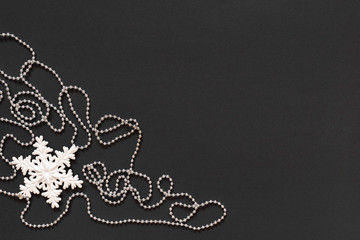 Holiday background , white snowflake and silver decorative beads on black background, flat lay, top view