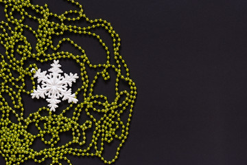 Holiday background , white snowflake and green bright decorative beads on black background, flat lay, top view