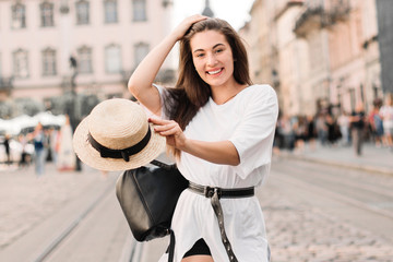 Young stylish woman walking on the old town street, travel with backpack, straw hat, wearing trendy outfit.