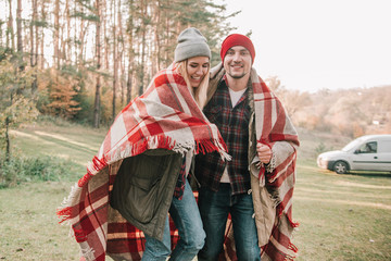 Couple huggings travelers covered with plaid in the forest. Concept of trekking, adventure and seasonal vacation.