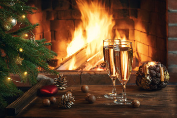 Christmas composition - Two glasses with champagne on a wooden table near a Christmas tree in a room with a burning fireplace