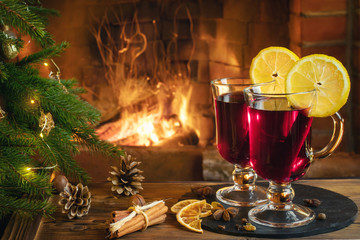 Christmas composition - two glasses with mulled wine on a wooden table near a Christmas tree opposite a burning fireplace