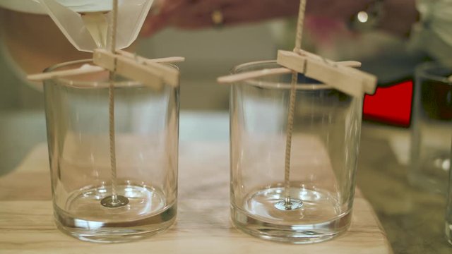 Close up of hot wax pouring in slow motion into empty candle glass next to an empty glass