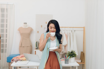 Young fashion designer on her atelier making a pause and drinking coffee