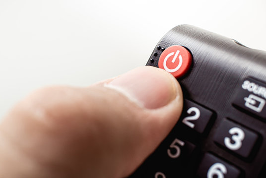 Photograph of a hand holding a television remote control pretending to be about to push the power button