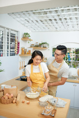 Couple man and woman wearing aprons having fun while making homemade pasta in kitchen at home