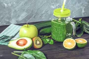 healthy green smoothie with ingredients on a wooden table: apple, kiwi, lime, spinach, mint, avocado, cucumber