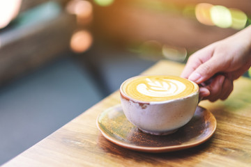 A woman holding a cup of hot latte coffee on wooden table in the morning