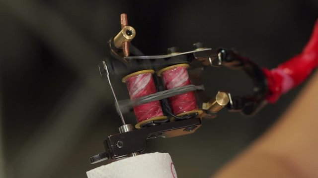 Close-up of a tattoo machine in motion while applying a tattoo to the skin. A working tattoo machine with many needles. Slow motion.