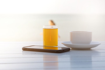 Tea coffee with smart phone on the white wooden table at the beach