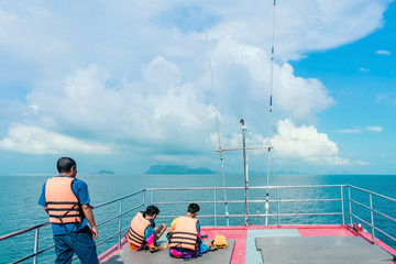Tourists relaxing on boat deck and looking to the beautiful tropical island on hot sunny day.