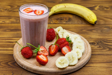 Glass of fresh smoothie of strawberry and banana on a wooden table
