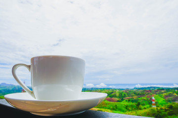 White hot coffee mugs placed on a wooden floor with green fresh mountain and morning fog as background