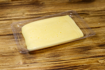Slices of cheese in disposable plastic packing box on wooden table